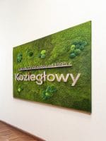 Napis z nazwą firmy wykonany z litego dębu, umieszczony na zielonym panelu z mchu stabilizowanego.