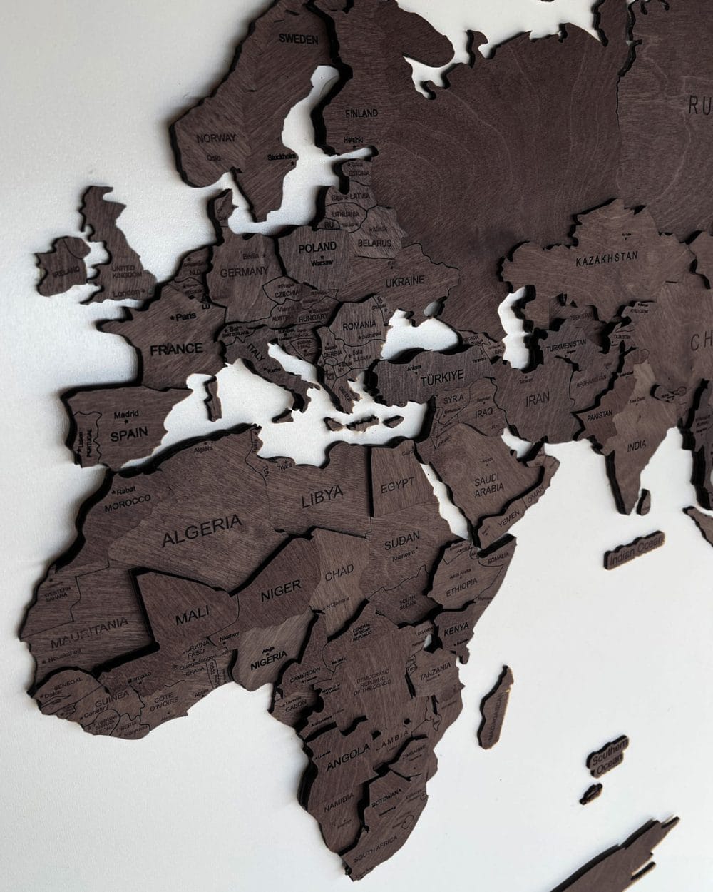 Drewniana mapa świata 3D w kolorze czekolady zawieszona na białej ścianie.
